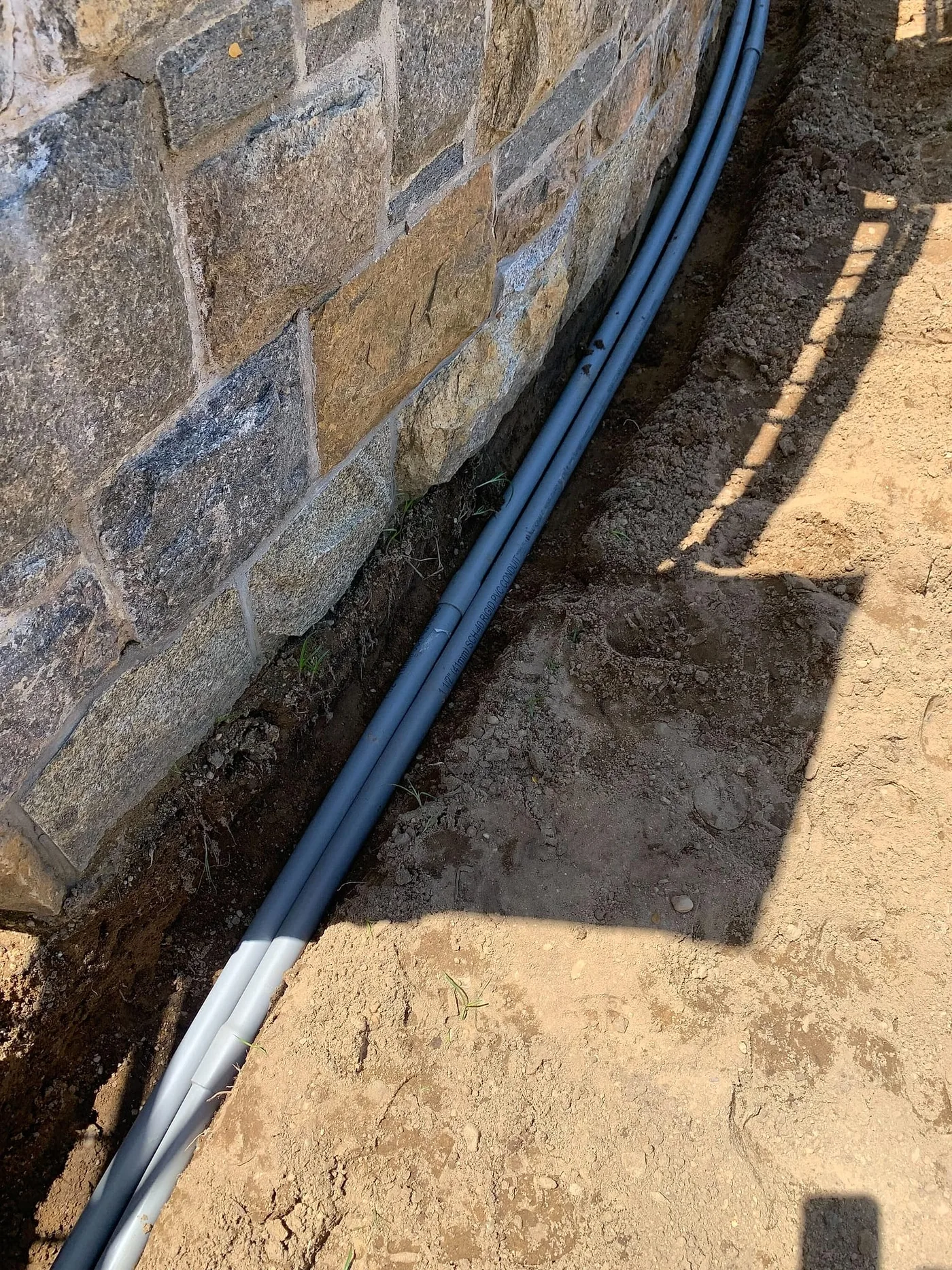 Conduit laid along a stone retaining wall before backfill