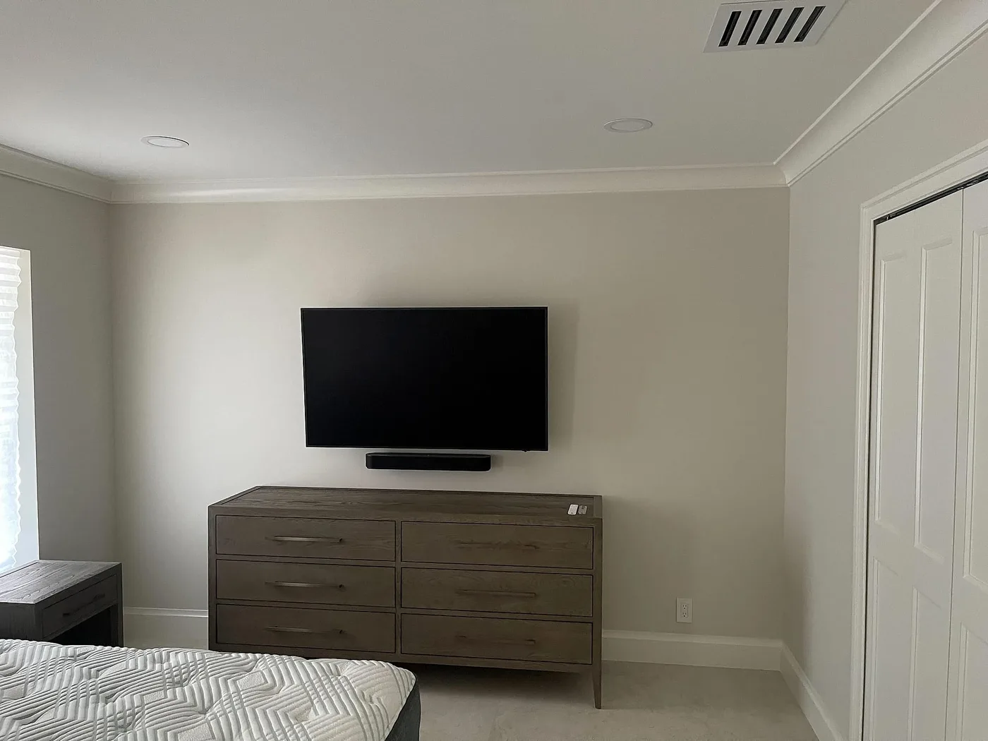 Bedroom with a wall-mounted television above a dresser, screen off